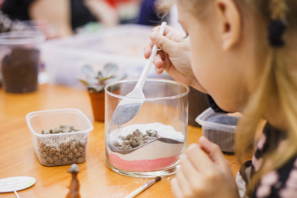 Detailed view of hands creating distinct colored sand layers using a paper funnel, showing the precision technique for achieving clean, sharp divisions between each colored layer