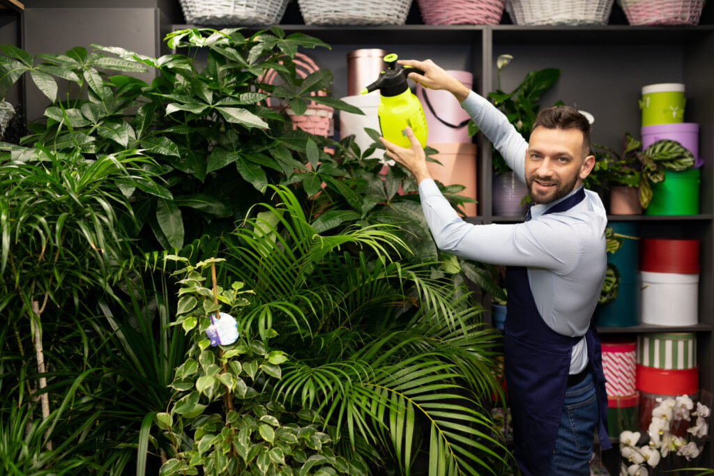 Person assembling a wooden corner plant shelf system with tools, measuring tape, and plants waiting to be arranged on the completed structure