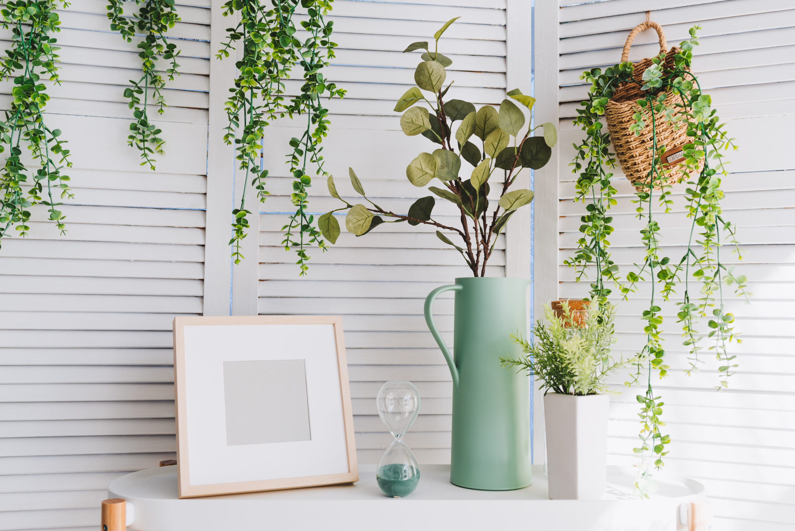 Modern gallery wall featuring framed artwork in various sizes interspersed with small built-in shelves displaying potted plants and trailing vines that complement the art pieces